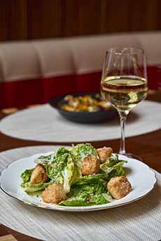 A plate of Caesar salad with a glass of white wine