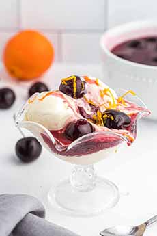 A glass dish of Cherries Jubilee garnished with orange zest.