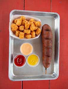 A tray with a Corn Dog, Tater Tots, and condiments: ketchup, mustard, and Russian dressing.