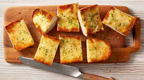 A wood cutting board with slices of garlic bread.