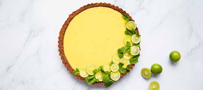 Key lime pie with a chocolate nut crust, garnished with lime slices and mint leaves.
