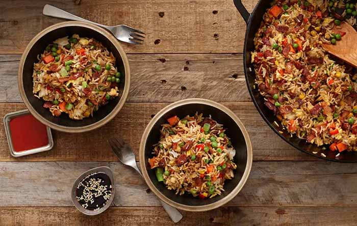 A wok and two bowls of bacon fried rice.