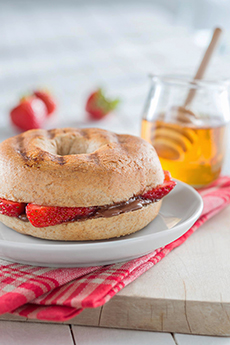 A bagel with fresh strawberries and honey