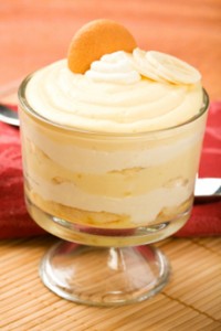 A glass pedestal serving dish with banana pudding, layered with whipped cream and Nilla wafers.