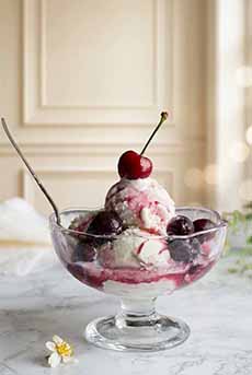 A glass dish of Cherries Jubilee on a marble dining table.