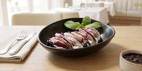 A bowl of dessert pierogi: a sweet cheese filling with blueberry sauce.