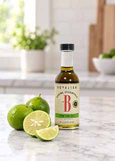A bottle of lime oil on a kitchen counter with fresh Key limes.