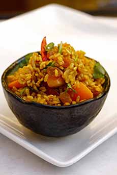 A bowl of fried rice, shrimp, and dried apricots, using brown rice.
