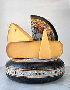A whole wheel of Gouda cheese stacked with a half wheel and wedges