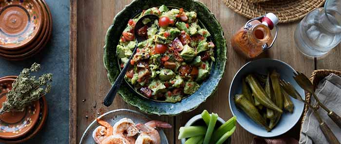 A bowl of Cajun Guacamole with sides of shrimp and okra.