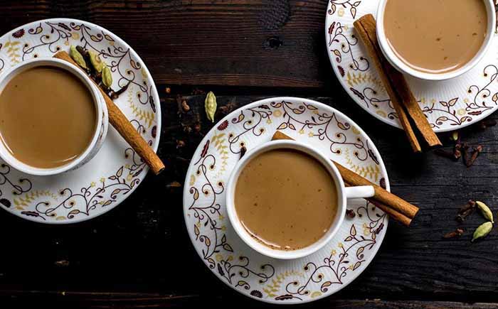 Three teacups of masala chai, garnished with cinnamon sticks.