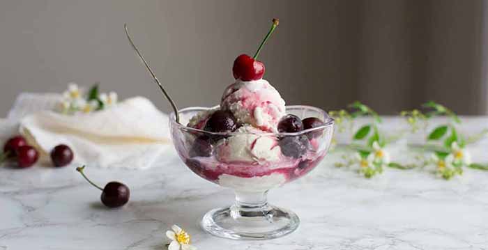 A stemmed dish of Cherries Jubilee on a marble tabletop.