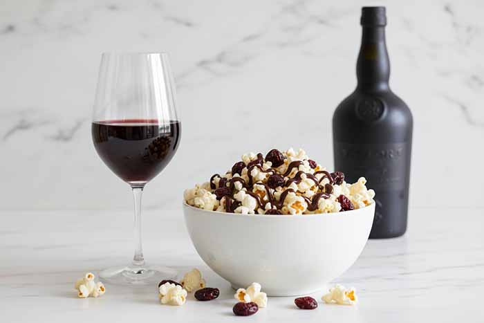 A bowl of chocolate-cherry popcorn with a glass of Ruby Port
