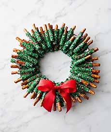 A Christmas wreath made of chocolate-covered pretzel rods with green sprinkles.