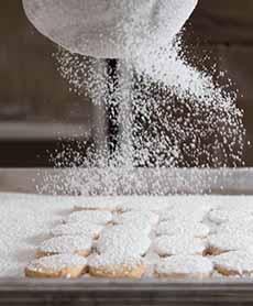 Sprinkling Confectioners Sugar On Donuts