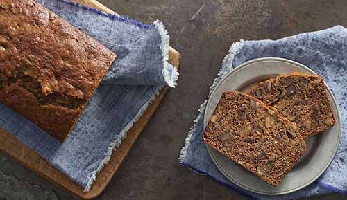 A loaf of date nut bread with two slices on a plate.