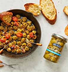 A pan of sauteed Castelvetrano olives with cherry tomatoes and crusty bread