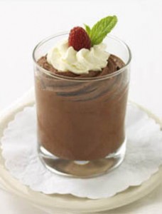 A glass dish of chocolate mousse topped with whipped cream, a raspberry, and a mint leaf.
