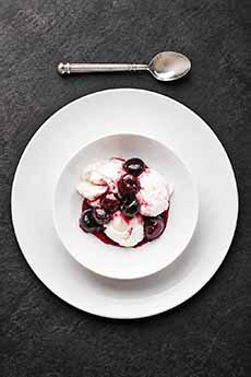 A simple white bowl and service plate with Cherries Jubilee.