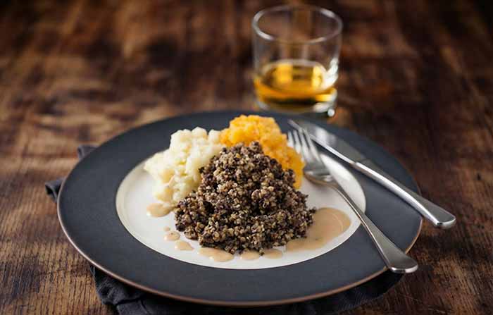 A plate of haggis, tatties, and neeps with a glass of Scotch