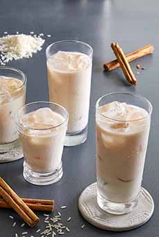 Several glasses of horchata with ice and cinnamon sticks.