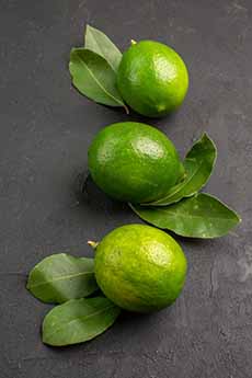 Three Key limes with their leaves on a counter.