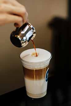 Pouring espresso into a cup of foamed milk to make a caffe macchiato.