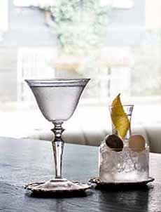 A Martini served with a small pitcher of ice and garnishes: olives and lemon peel.