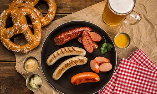 A tasting plate of different sausages, a beer, and a soft pretzel.