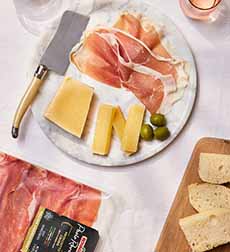 A plate of prosciutto and cheese with bread and green olives.