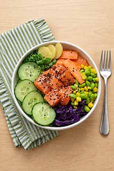 A salmon poke bowl with cucumbers, carrots, edamame, and corn.