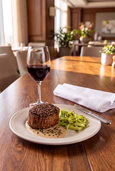 A plate of steak au poivre and a glass of red wine on a restaurant table.
