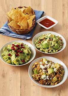 Three bowls of guacamole with different garnishes: pomegranate arils, cotija cheese, and diced avocado.