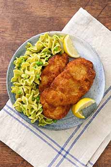 A plate of Wiener Schnitzel with buttered noodles and peas.